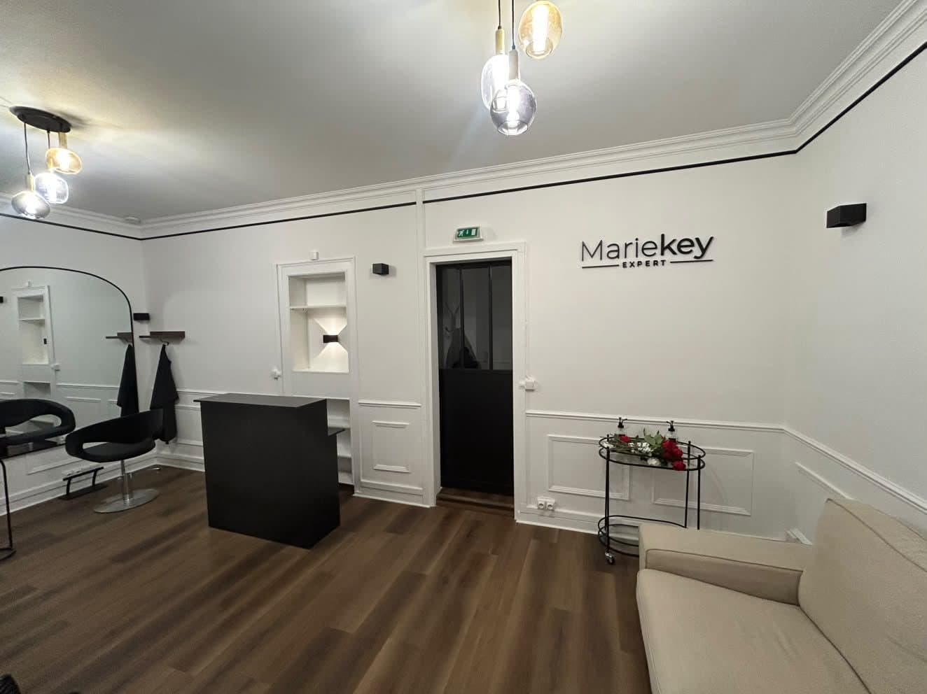 Accueil du salon : comptoir noir, canapé beige et enseigne Mariekey Expert